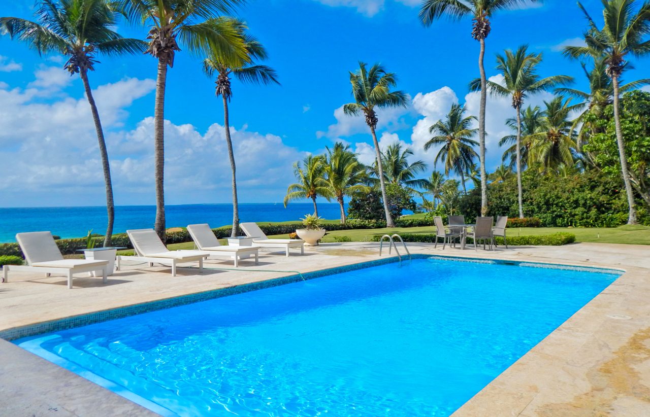 An oceanfront swimming pool with white loungers and palm trees in the Dominican Republic