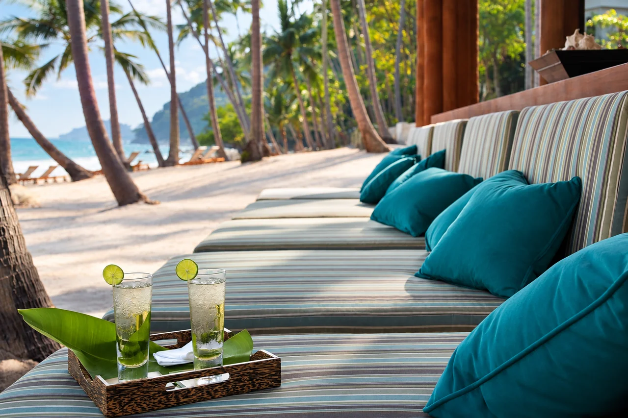 A beachfront daybed with teal cushions and two lime drinks in Koh Samui