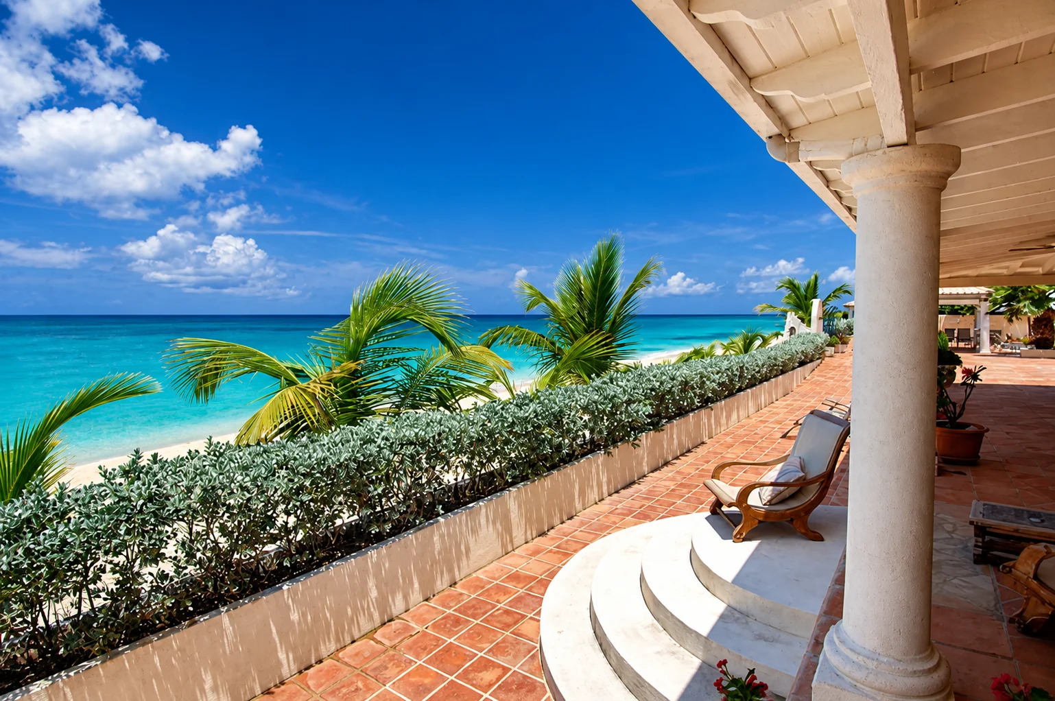 A seaside villa veranda with white columns and palms overlooking turquoise water in St. Barts