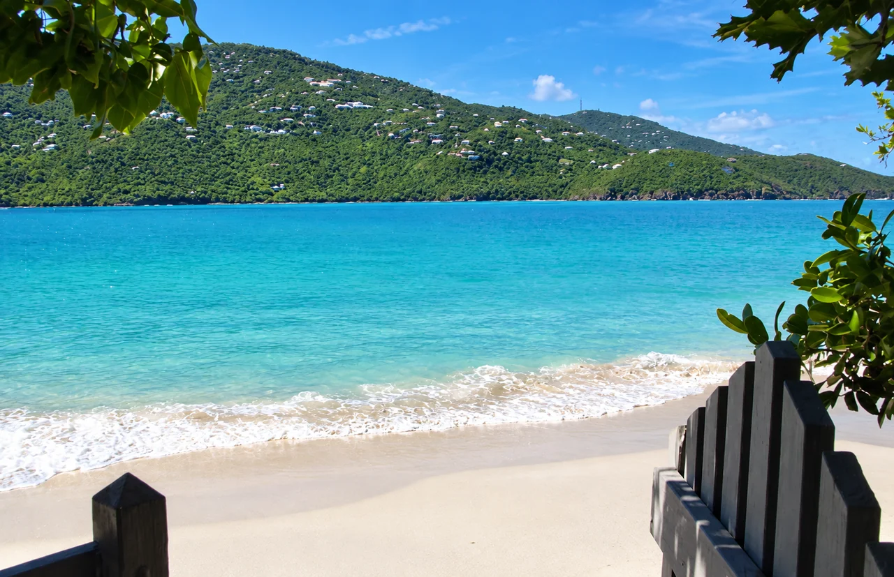 A beach gate overlooking calm turquoise water and a green hillside in St. Thomas
