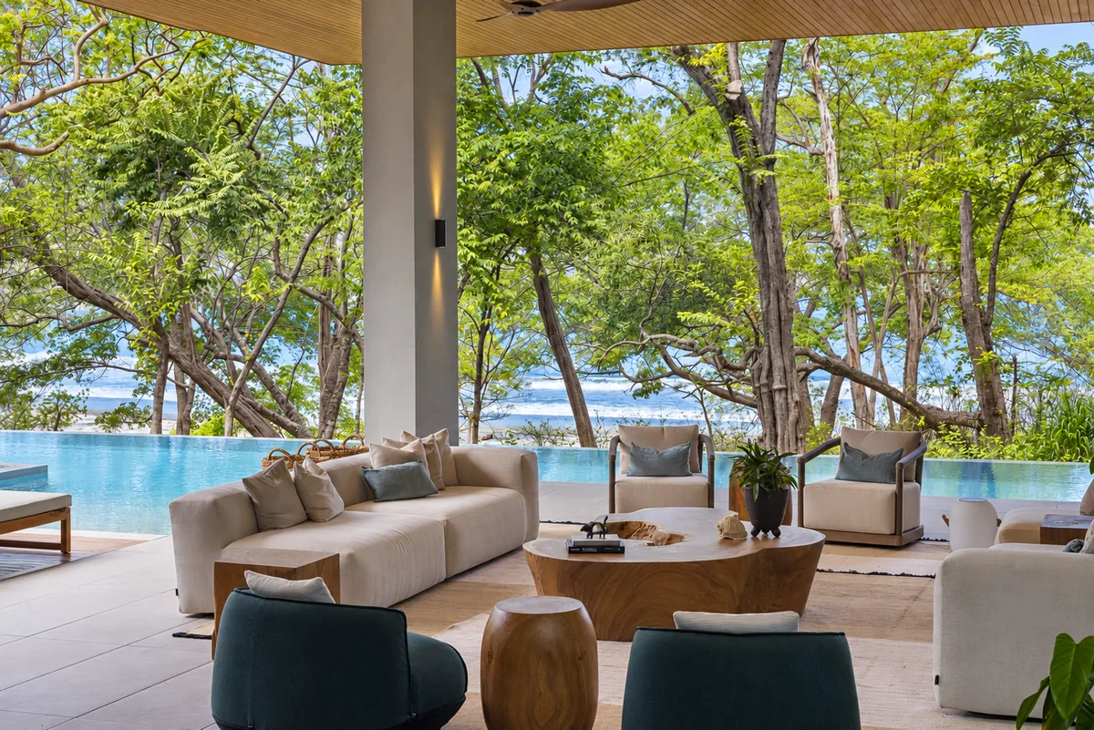 An open-air villa lounge beside a pool and trees overlooking the coast in Costa Rica